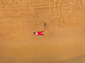 Aerial view of two girls having fun lying on the beach in Cajueiro, Brazil.