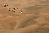 Luftaufnahme von Kamelen mit Männern auf den Sanddünen von Khuri, Jaisalmer, Rajasthan, Indien