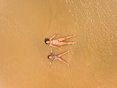 Aerial view of two girls having fun lying on the beach in Cajueiro, Brazil.