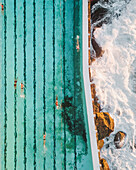 Aerial view of bondi icebergs swimming club with swimmers enjoying the turquoise ocean waves, Sydney, Australia.