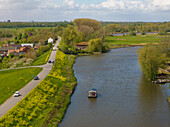 Aerial view of the tranquil Linge river with a boat and scenic countryside homes amidst greenery and trees, Betuwe, Netherlands.