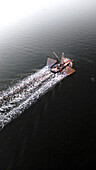 Aerial view of a trawler navigating the serene Wadden Sea at sunrise with seagulls overhead, Harlingen, Netherlands.