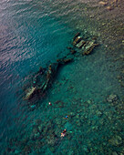 Aerial view of a beautiful beach with a shipwreck and people swimming in the clear sea, Amed, Bali, Indonesia.