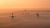 Aerial view of a mystical landscape with a windmill and church shrouded in fog at sunrise, Schermerhorn, Netherlands.