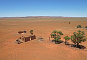 Aerial view of farm ruins in a vast arid landscape with scattered trees, Whyte Yarcowie, South Australia.