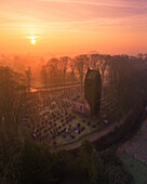Aerial view of a serene church and cemetery under a mystical sunrise with fog, Eastermar, Netherlands.