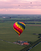 Aerial view of a hot air balloon floating over a picturesque countryside meadow at sunset, Joure, Netherlands.