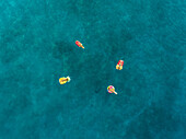 Aerial view of four friends floating on inflatable mattresses on Atokos island, Greece.