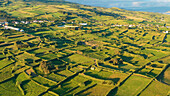 Luftaufnahme von üppig grünen Feldern und Hügeln, die ein malerisches Dorf am Meer umgeben, Horta, Portugal.