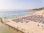 Aerial view of crowded beach with straw thatch parasols on Achaia, Greece.