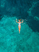 Aerial view of a woman floating in the sea of Atokos island, Greece