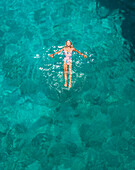 Aerial view of a attractive young woman in swimsuit floating in the sea off Atokos island, Greece