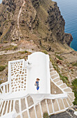 Aerial view woman lying on roof on Santorini traditional house with sea in background, Greece.