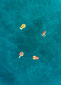Aerial view of four friends floating on inflatable mattresses on Atokos island, Greece.
