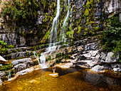 Aerial view of a woman standing in front of a waterfall in black swimsuit, Rawsonville, Western Cape, South Africa.
