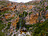 Aerial view of a woman standing in front of a waterfall in black swimsuit, Rawsonville, Western Cape, South Africa.