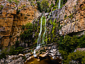 Aerial view of a woman standing in front of a waterfall in black swimsuit, Rawsonville, Western Cape, South Africa.