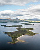 Aerial view of serene Loch with a picturesque island and majestic mountains under a calm sky, Alexandria, Scotland.