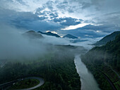 Luftaufnahme des ruhigen Flusses Enns, der sich durch üppig grüne Täler und majestätische Berge unter einem nebligen Himmel schlängelt, Sankt Gallen, Österreich.