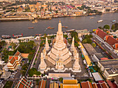 Aerial view of Wat Arun Pagoda along the Chao Phraya river at sunset with urban residential district in background, Khet Phra Nakhon district, Bangkok, Thailand.