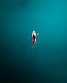 Aerial view of woman surfing with red surfboard in blue ocean, Primorje-Gorski Kotar, Croatia.