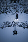 Snowy evening aerial view of a car stopping on a dam next to a river and lake in Estonia.