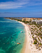Aerial view of people on the beach along the shoreline with hotel buildings in Palm Beach in Aruba.