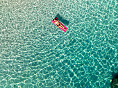 Aerial view of mariolu beach with a woman on an inflatable mattress in turquoise water, Baunei, Italy.