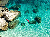 Luftaufnahme des Strandes Mariolu mit einer Frau auf einer aufblasbaren Matratze im türkisfarbenen Wasser, Baunei, Italien.