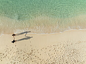 Luftaufnahme von Menschen, die an einem Sandstrand mit klarem Wasser und Wellen spazieren gehen, North Eleuthera, Bahamas.