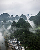 Aerial view of serene karst mountains shrouded in fog with a picturesque village nestled in the valley, Guilin, China.