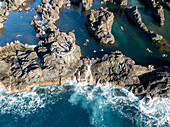 Aerial view of rocky shoreline with natural pools and tranquil blue water, Ilheus da Janela, Madeira, Portugal.