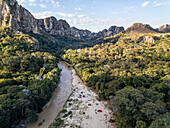 Luftaufnahme eines gewundenen Flusses, umgeben von üppigem Grün und majestätischen Bergen mit Zelten in einem ruhigen Tal, Toliara - Tulear, Madagaskar