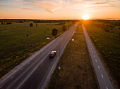 Aerial view of a car driving on a road at sunset in countryside.