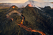 Luftaufnahme von Lava, die den Bergrücken hinunterfließt, Blick auf einen Lavastrom, der aus den Kratern in Grindavík, Südliche Halbinsel, Island, fließt