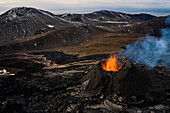 Aerial view of a volcano smoking from the crater, view of magma erupting from the crater with mountains landscape in background, Grindavík, Southern Peninsula, Iceland.