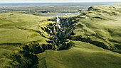 Luftaufnahme der atemberaubenden Fjadrargljufur-Schlucht mit üppig grünem Grasland und einem ruhigen Fluss, Skaftarhreppur, Island