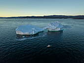 Aerial drone view a huge iceberg with an arch surrounded by a red boat, Ilulissat, Greenland, Arctic.