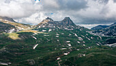 Aerial view of rugged snowy mountains and a serene valley under a cloudy sky, Durmitor National Park, Montenegro.