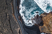 Luftaufnahme von oben auf das Wasser des Ozeans, das entlang der Küstenlinie am schwarzen Sandstrand des Lago Verde (Grüner See), Lanzarote, Kanarische Inseln, Spanien, bricht