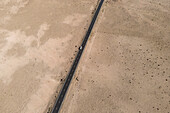 Luftaufnahme einer Straße, die ein sandiges Wüstental auf Lanzarote, Kanarische Inseln, Spanien, durchquert, von oben.