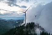 Aerial view of majestic wind turbines amidst clouds and mountains in a scenic landscape, Voitsberg, Austria.