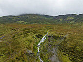 Luftaufnahme eines atemberaubenden Wasserfalls, der durch ein üppig grünes Tal stürzt, umgeben von majestätischen Bergen, Portree, Vereinigtes Königreich