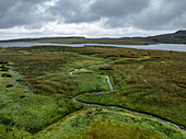 Luftaufnahme einer ruhigen und malerischen Landschaft mit einem Fluss, der sich unter einem bedeckten Himmel durch üppig grüne Hügel schlängelt, Portree, Schottland.