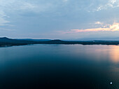 Luftaufnahme des ruhigen Viverone-Sees bei Sonnenuntergang mit schönen Reflexionen und heiteren Wolken, Viverone, Italien.