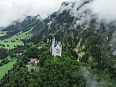Aerial view of neuschwanstein castle surrounded by majestic mountains and lush forest under cloudy skies, Hohenschwangau, Germany.
