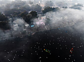 Aerial view of serene Yamuna Ghat with boats and birds amidst mist and low clouds, New Delhi, India.