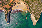 Aerial view of a beach area with umbrellas in a secluded cove only accessible by boat on the rocky coastline of Albufeira, Algarve, Portugal.