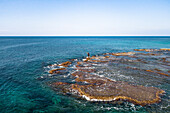 Luftaufnahme eines Mannes, der mit einer Angelrute fischt, während er auf Felsen im Meer steht, Akko, Israel.