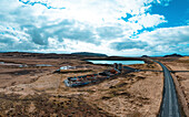 Aerial view of abandoned building, road, sky, clouds, lake, and mountains, Grindavik, Iceland.